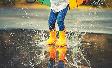 Girl splashing in a puddle with yellow wellies.