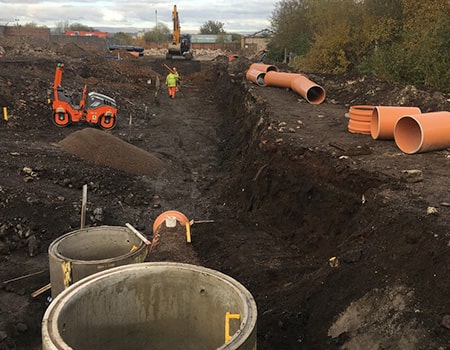 A view of a drainage trench with concrete manhole and ULTRA3 pipe on the ground.