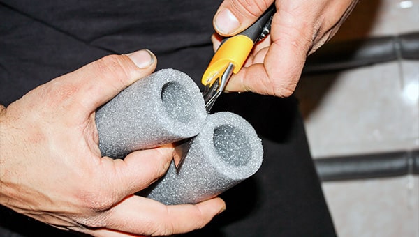 Person cutting foam lagging with a retractable blade knife.