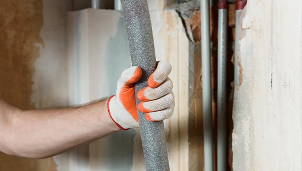 Person with gloves holding grey foam pipe lagging.