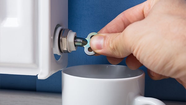 A person holding a key and bleeding a radiator into a white cup.