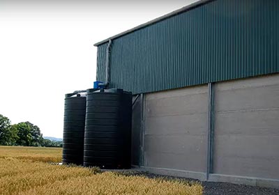 Two large rainwater storage tanks installed at an agricultural building.